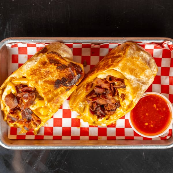 Two golden-brown burritos filled with macaroni and cheese and bacon, served with red sauce.