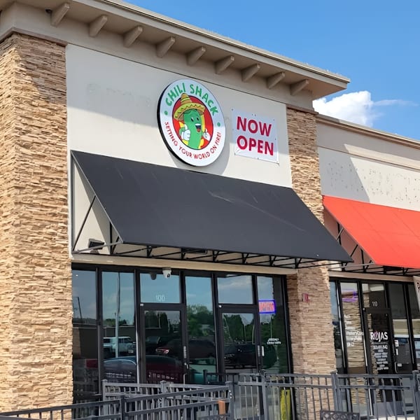 Exterior of Chili Shack restaurant with a black awning, stone facade, and "Now Open" sign.