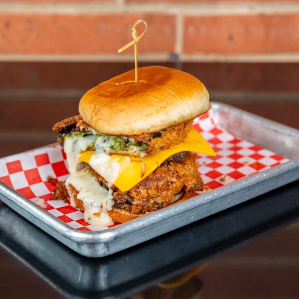 A double-patty burger with melted cheese and green sauce on a red and white checkered paper.
