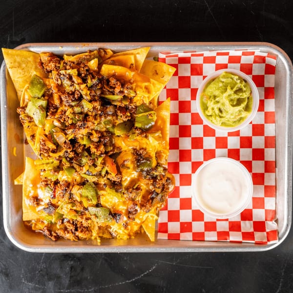 Loaded nachos with ground meat, green peppers, and cheese, served with guacamole and sour cream.