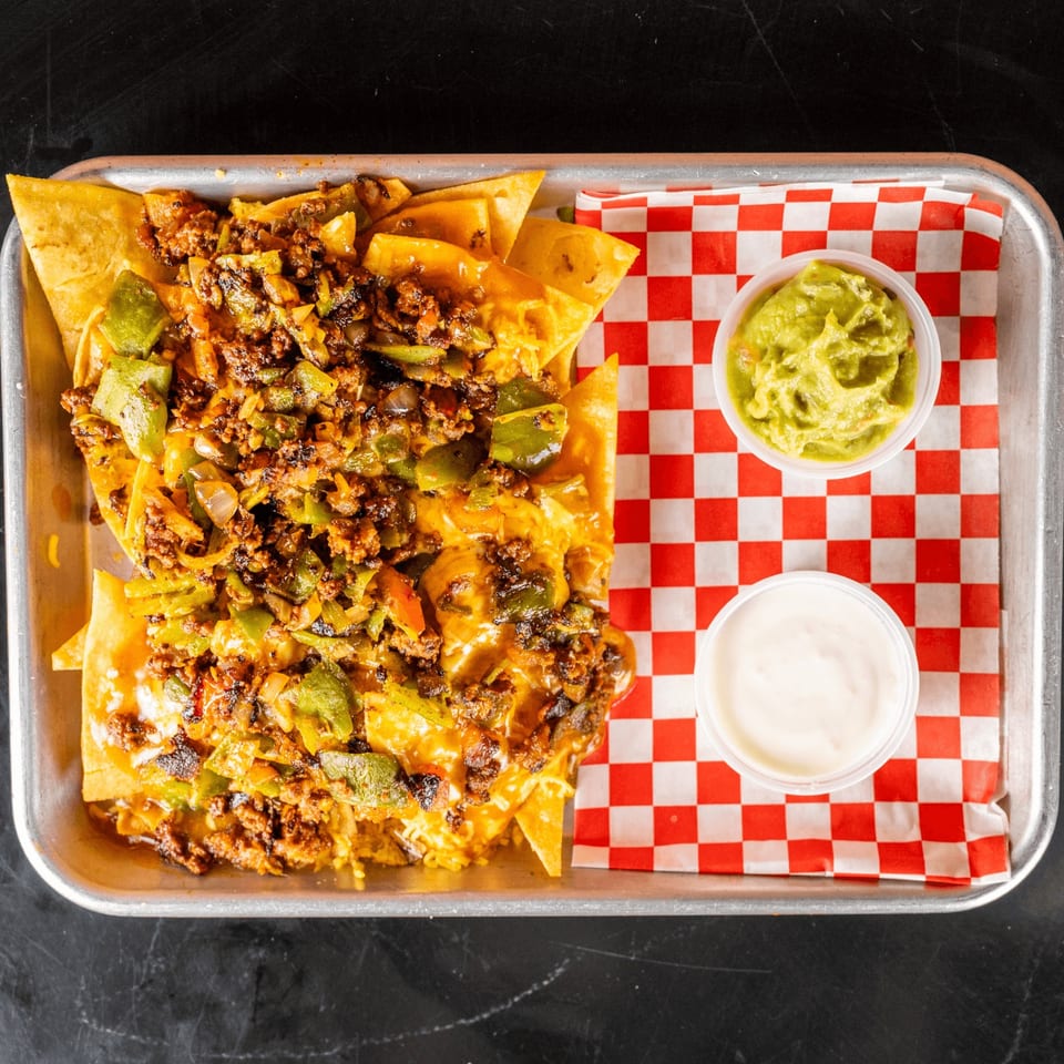 Loaded nachos with ground meat, green peppers, and cheese, served with guacamole and sour cream.