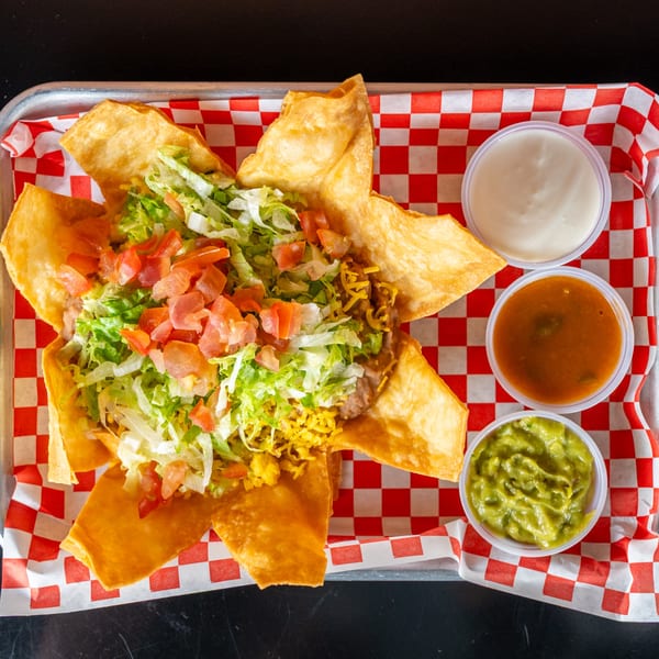 A taco salad in a crispy tortilla bowl with lettuce, tomatoes, and cheese, served with guacamole, salsa, and sour cream.