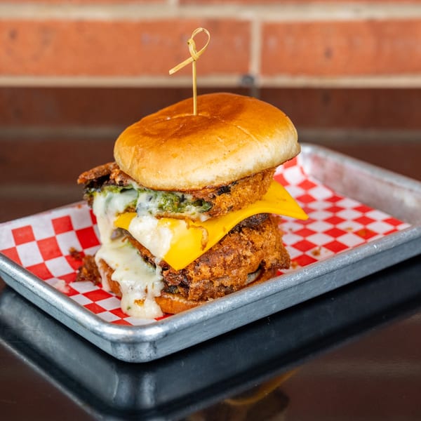 A double-patty burger with melted cheese and green relish on a red and white checkered paper.