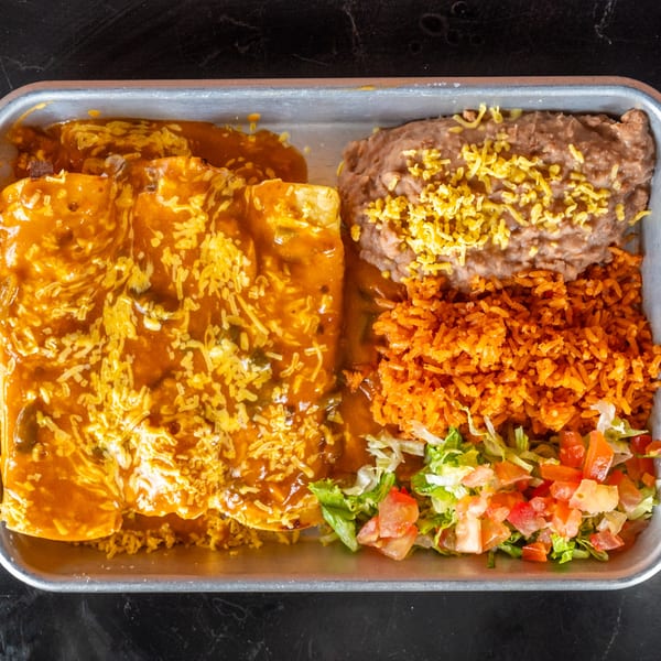 A metal tray holds enchiladas covered in orange sauce and cheese, with refried beans, rice, and salad.