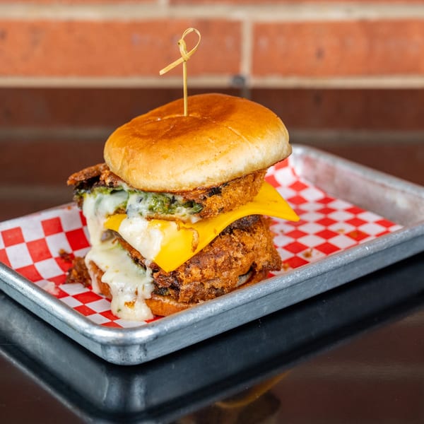A fried chicken sandwich with melted cheese and green sauce on a red and white checkered paper.