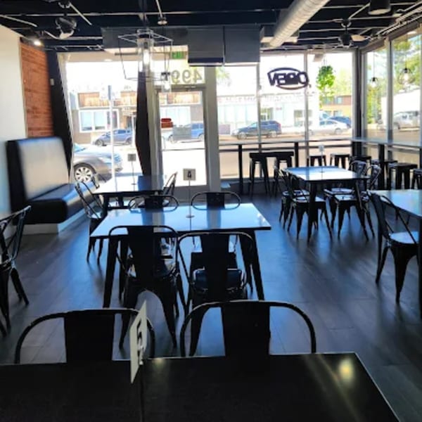 Interior of Chili Shack with black tables, chairs, and booths, large windows, and dark wood floors.