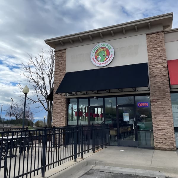 Exterior of Chili Shack restaurant with a black awning, stone facade, and outdoor patio seating.
