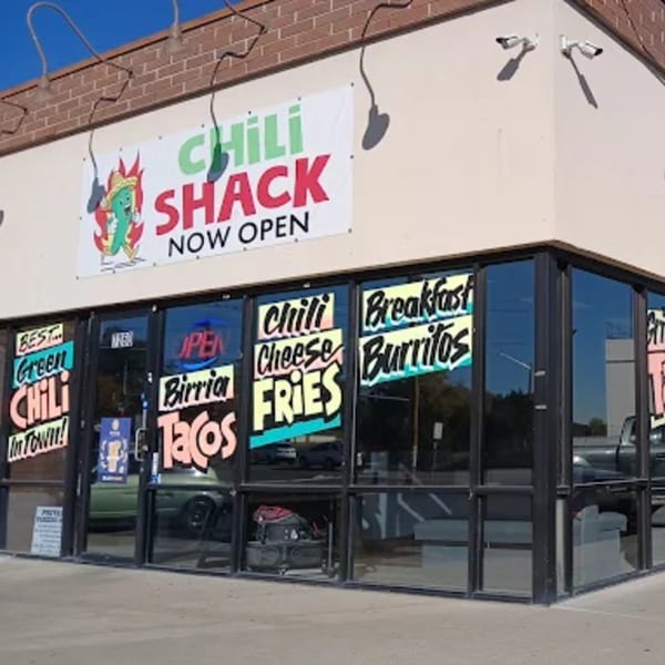 Exterior of Chili Shack restaurant with "Now Open" banner and window signs for Mexican food.