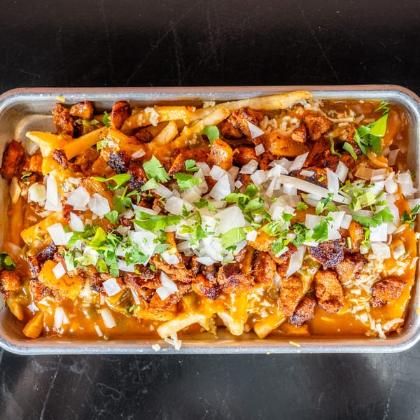 A metal tray of loaded fries topped with chicken, cheese sauce, white onions, and cilantro.