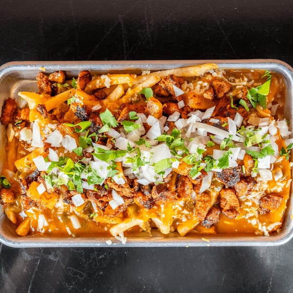 Overhead view of loaded fries with cheese, meat, onions, and cilantro in a metal tray.