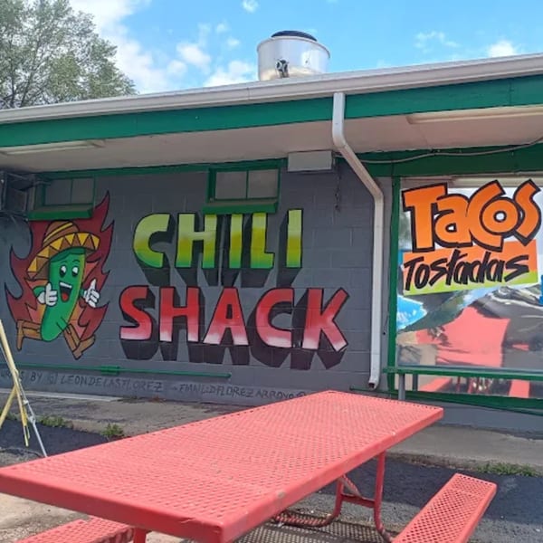Exterior of Chili Shack with a red picnic table, mural of a chili pepper, and "Tacos Tostadas" sign.