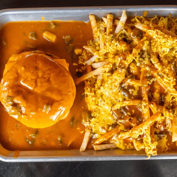 A burger covered in orange chili and cheese, next to chili cheese fries on a metal tray.