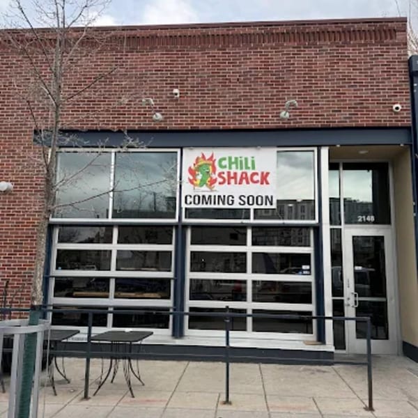 Chili Shack "Coming Soon" banner on a brick building with large windows and outdoor tables.
