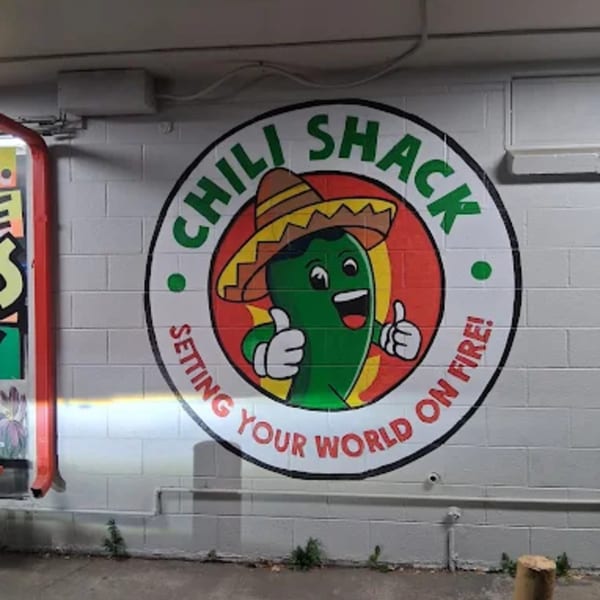 Chili Shack logo on a white brick wall, featuring a cartoon chili pepper in a sombrero.