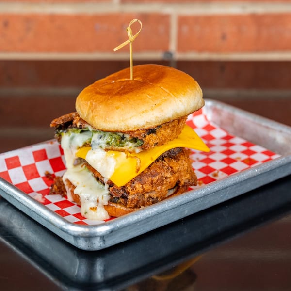 A double-patty burger with melted cheese and green sauce on a red and white checkered paper.